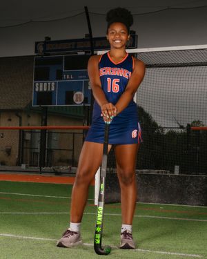 Female athlete in Hershey field hockey uniform on turf field, holding stick, team photo day by SportsFox Photography.