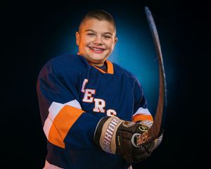 Youth hockey player in Hershey Hockey jersey, holding stick and smiling, dramatic lighting, team photo day by SportsFox Photography.