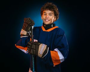 Youth hockey player in Hershey Hockey jersey, holding stick and smiling, dramatic lighting, team photo day by SportsFox Photography.