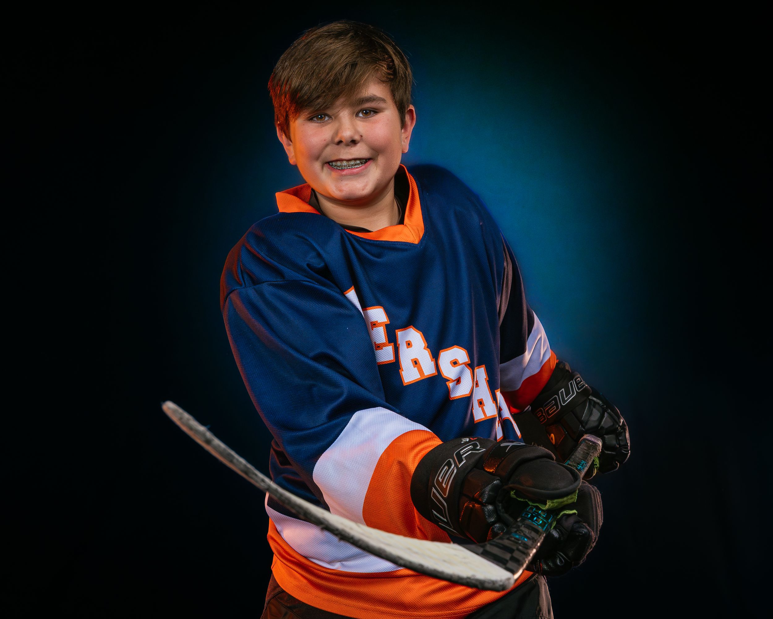 Youth hockey player in Hershey Hockey jersey, holding stick and smiling, dramatic lighting, team photo day by SportsFox Photography.