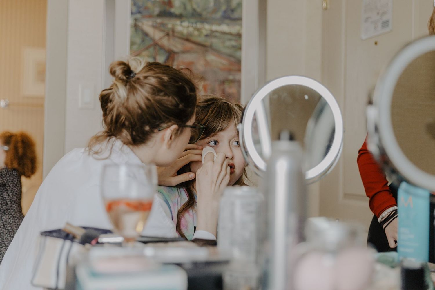 Makeup artist carefully applying eye makeup to bride at vanity mirror during wedding day preparations.