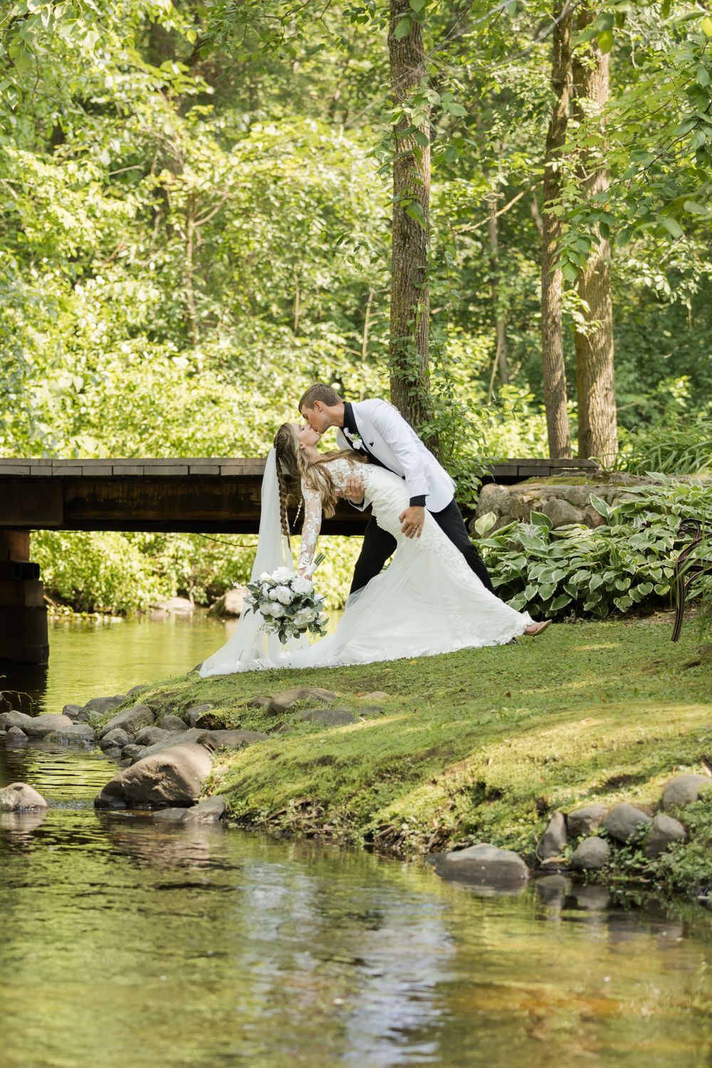 Romantic couple poses for photos near a stream in a lush garden setting.