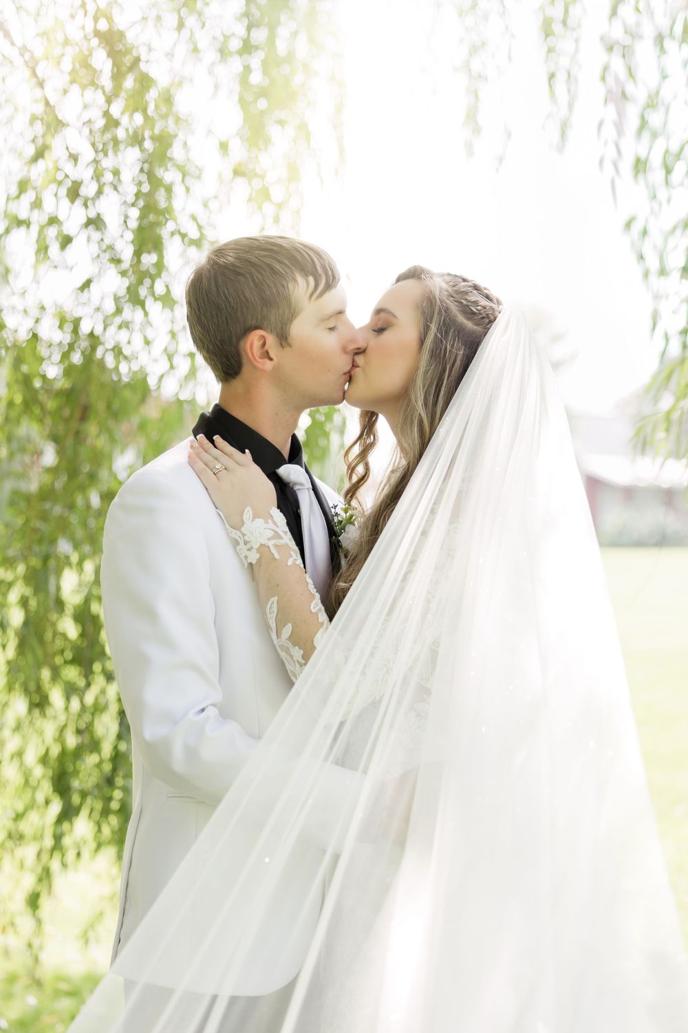 Romantic moment under willow tree branches with flowing white veil.