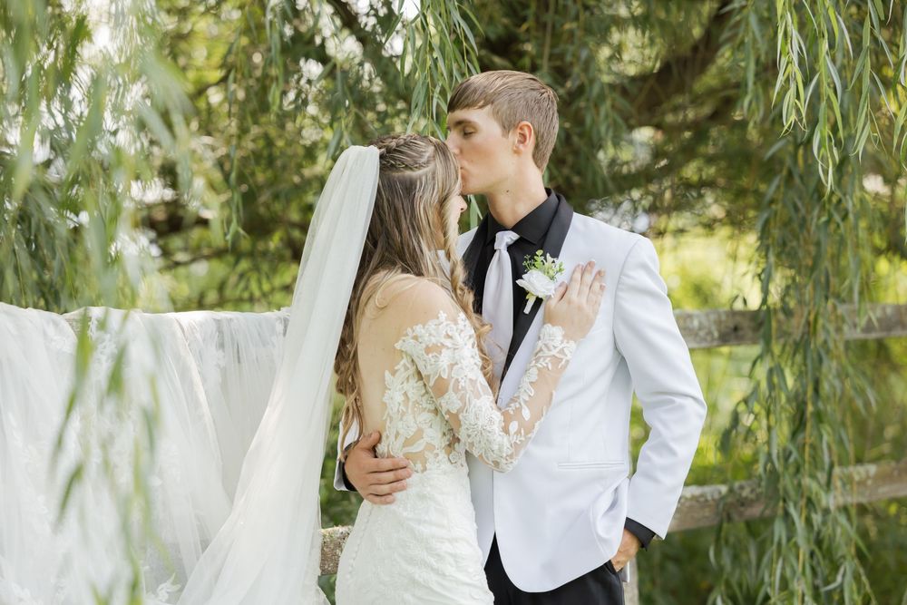 Elegant couple embraces under willow tree in wedding attire.