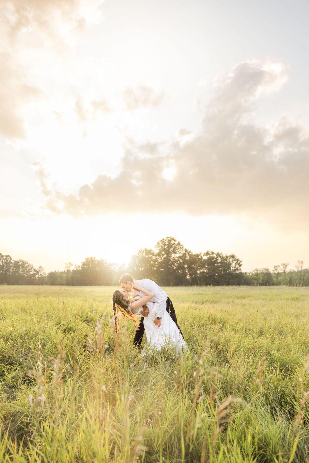 A romantic sunset photoshoot in a golden meadow with tall grass and trees in the background.