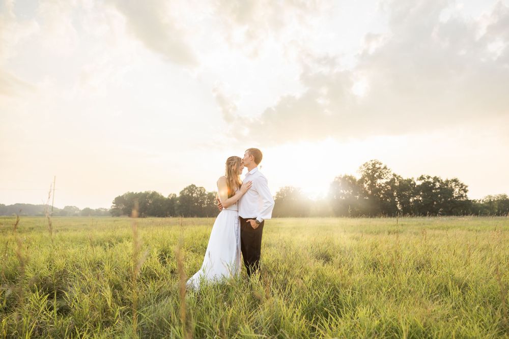 Couple embracing in a sun-drenched field during golden hour with dramatic lighting.