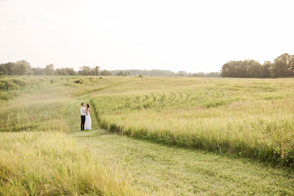 Long distance view of a couple in formal attire standing in a vast grassy field.