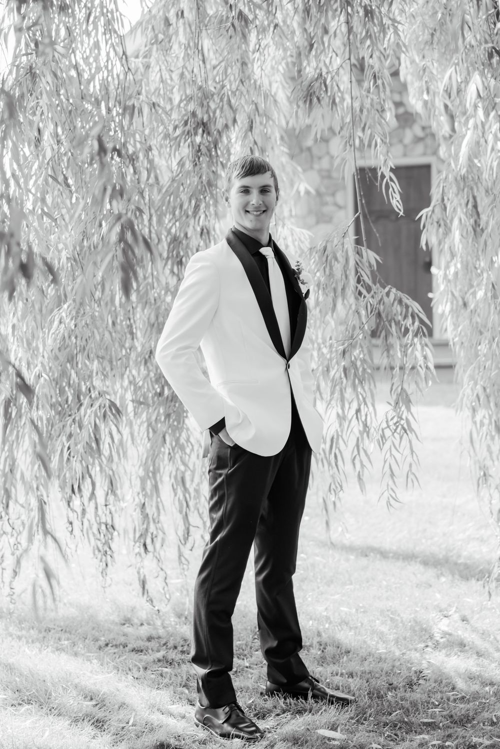 Black and white portrait under willow trees showing formal attire details.