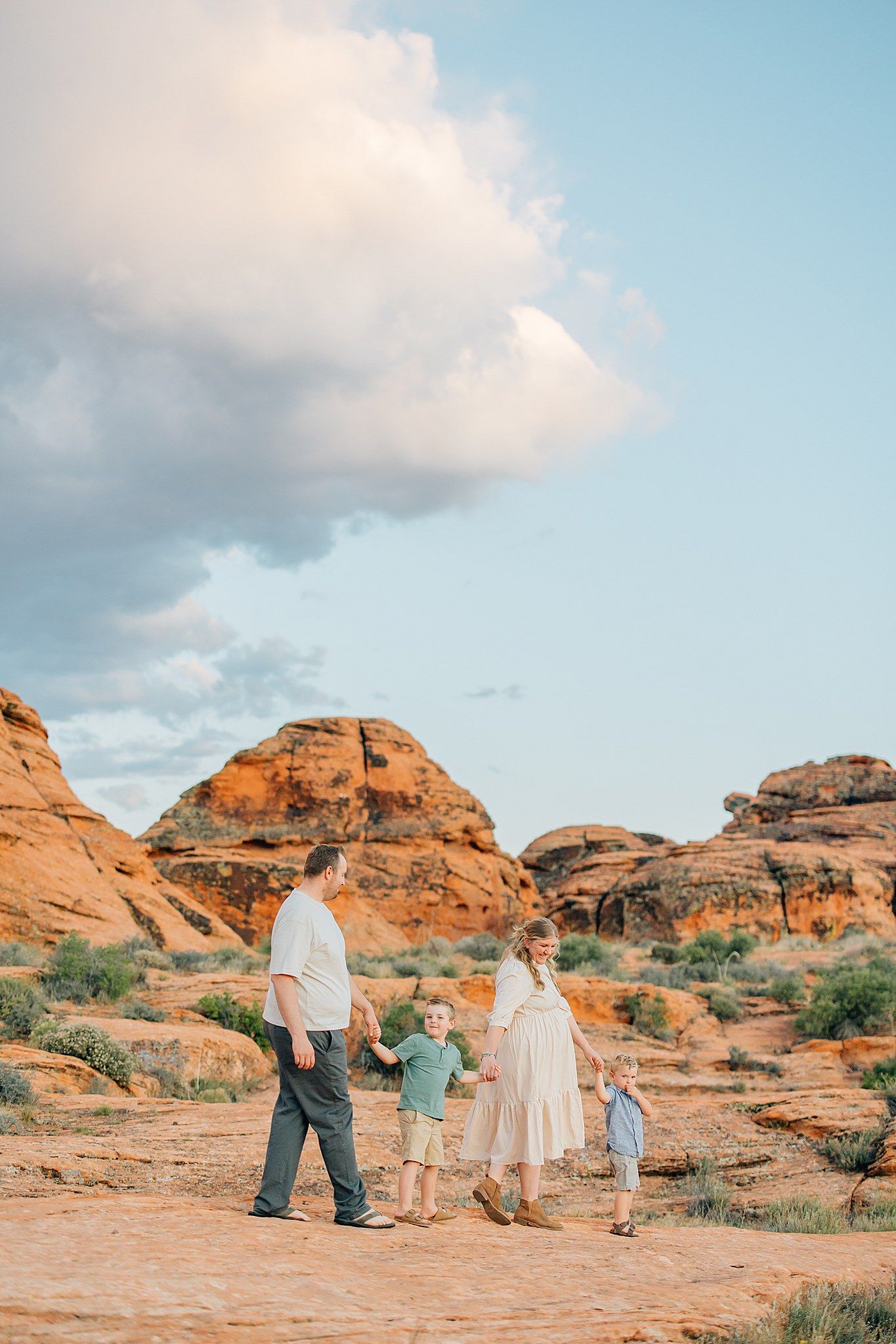 Family group walking together across scenic red rock desert formations under a blue sky with white clouds.