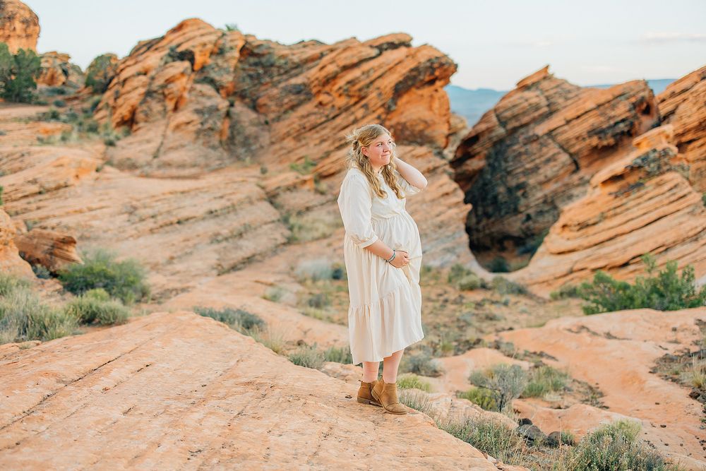 A person in a white dress stands on red sandstone formations at Valley of Fire State Park in Nevada.