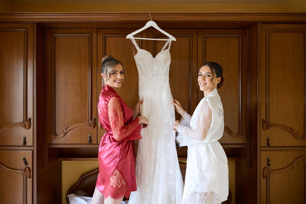 A wedding dress hangs elegantly in a rustic wooden room alongside a pink bridesmaid gown.