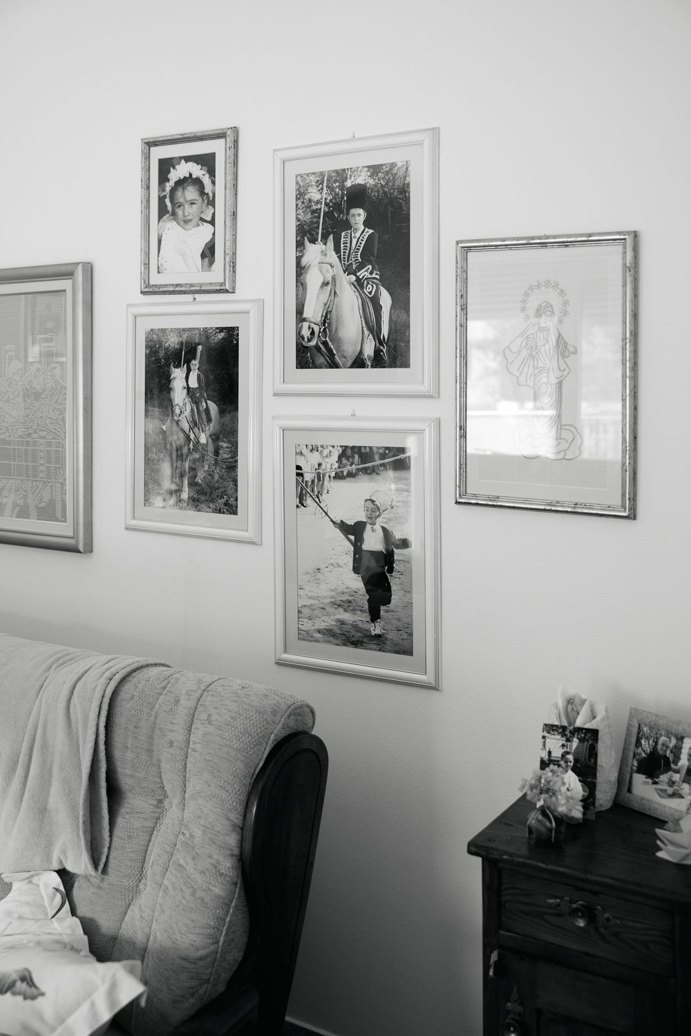 A panoramic view of framed photographs hanging on a white wall above a gray couch in a living room setting.