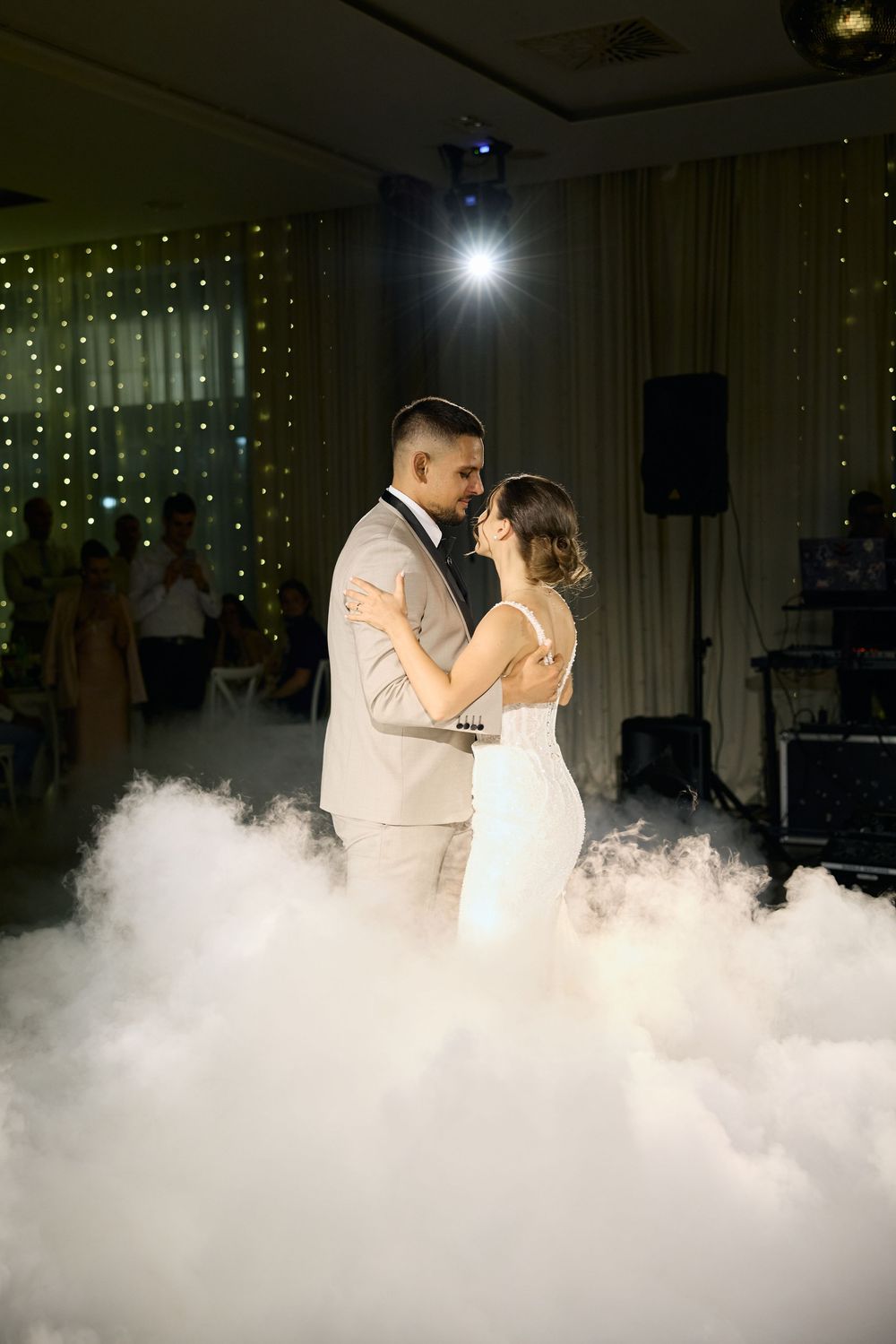 A couple shares their first dance surrounded by dramatic fog effects on a wedding reception dance floor.