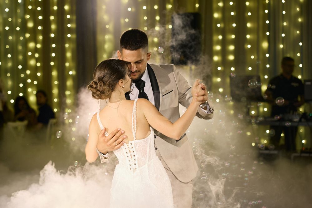 A couple shares their first dance as newlyweds on a misty dance floor with twinkling lights in the background.