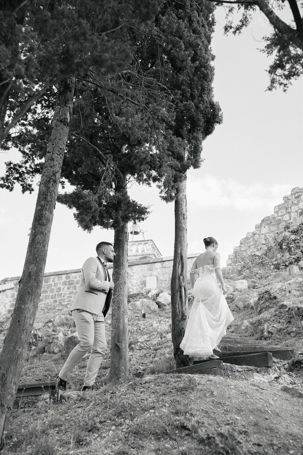 Black and white photos of a couple walking together on a hillside path among trees.