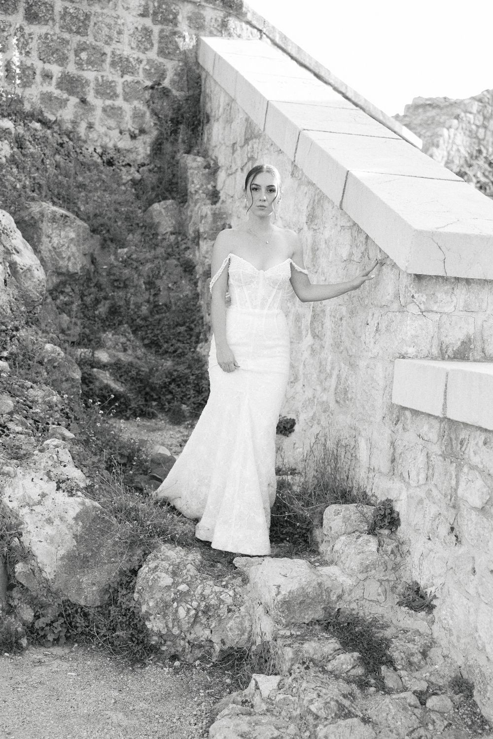 A series of black and white photos showing a bride in a white dress against a stone wall.