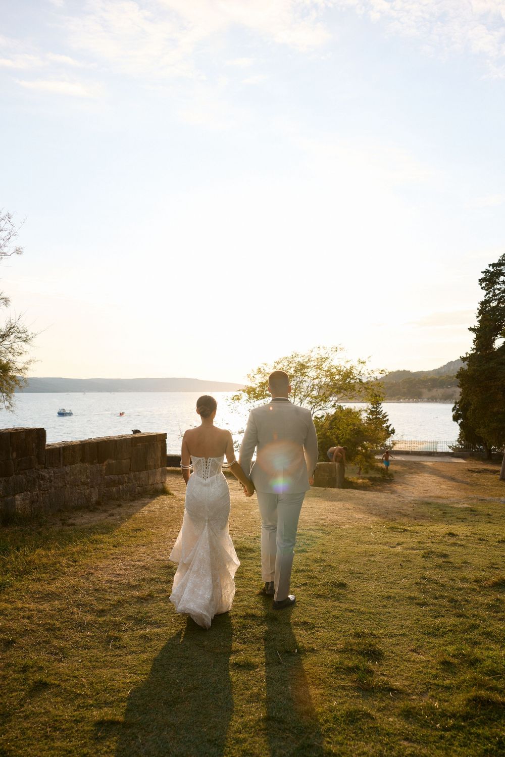 Silhouetted couple walks hand in hand along a coastal path at sunset with water views in the background.