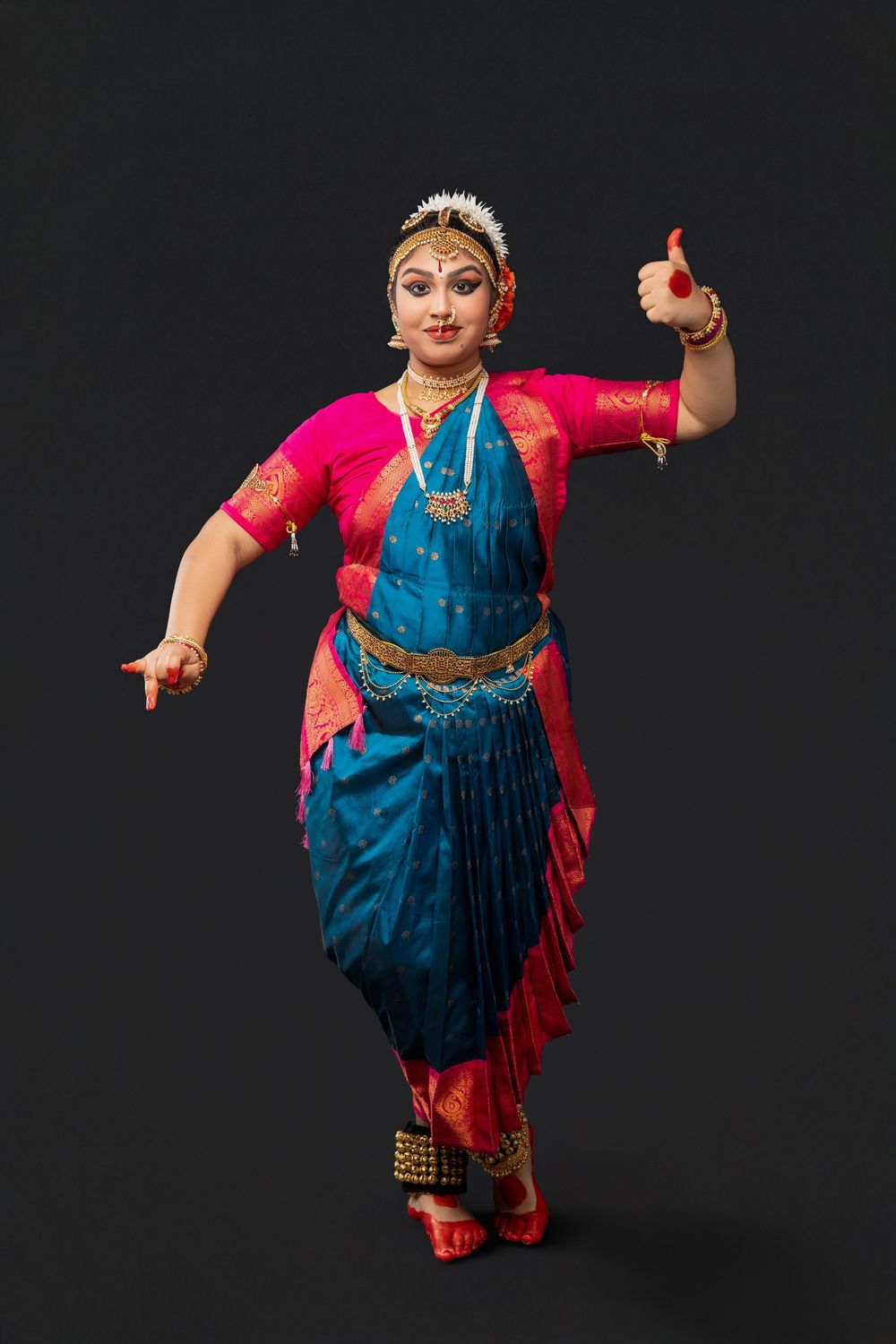 Classical Indian dancer performs in traditional blue and pink bharatanatyam costume against dark background.