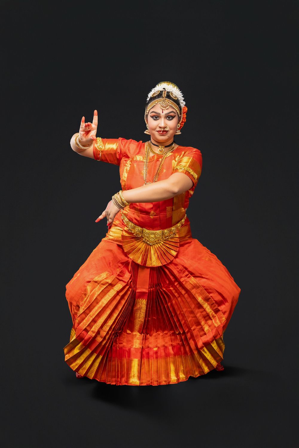 Bharatanatyam dancer in orange sari demonstrates graceful movements in traditional dance pose.