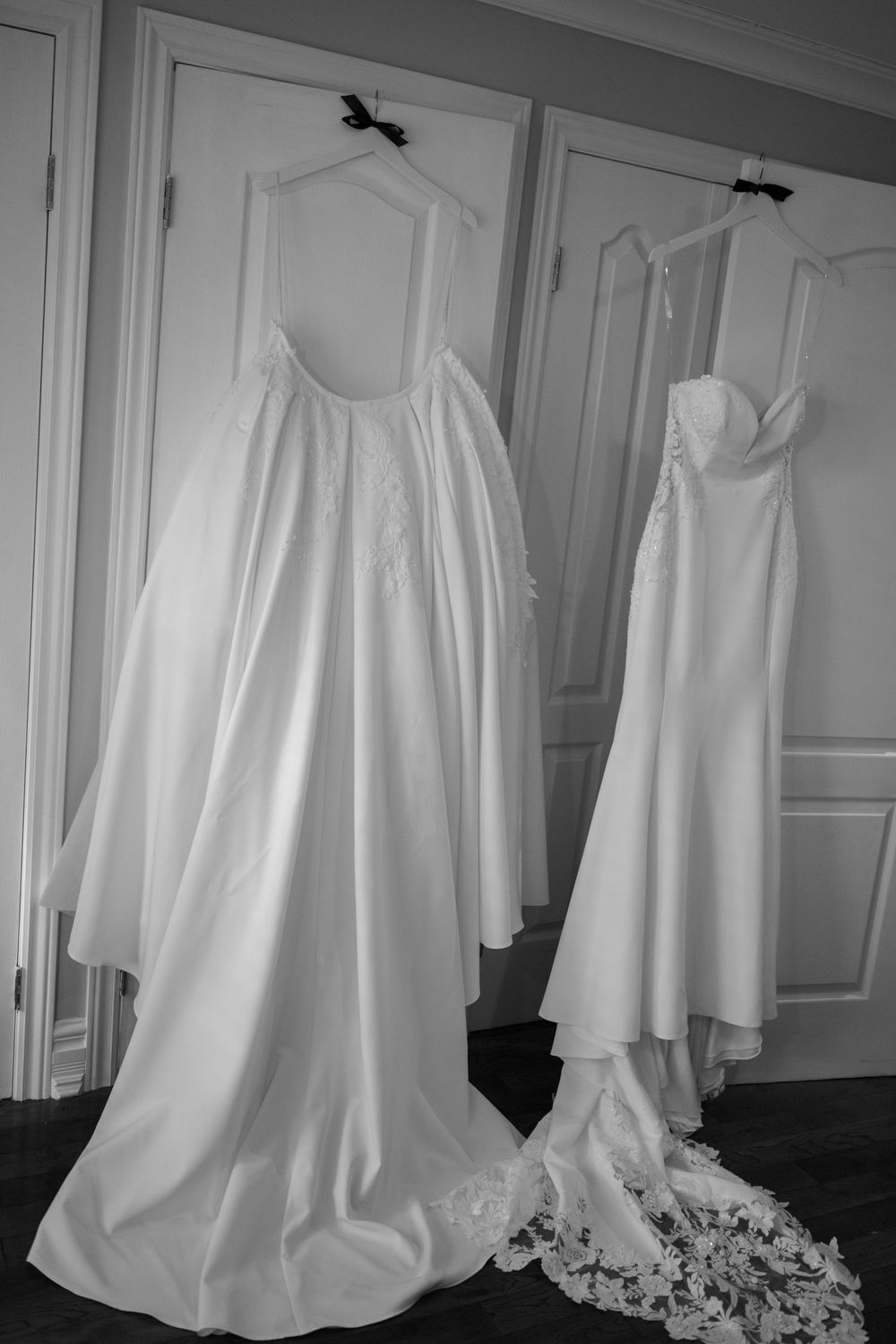 Wedding dress detail shots showing elegant white gown with flowing fabric and train against white paneled wall.
