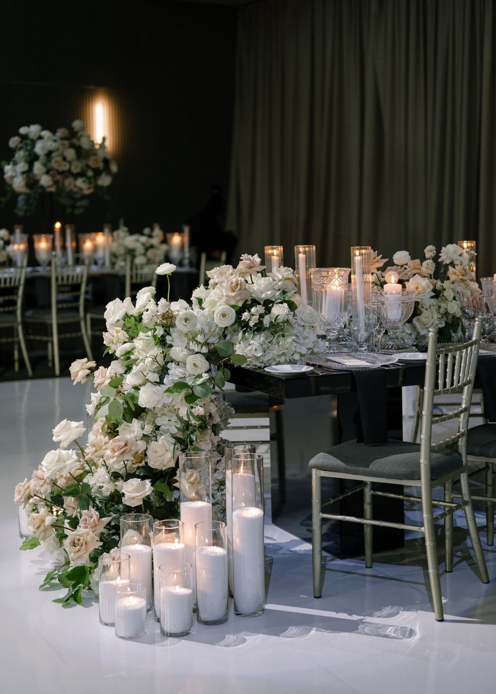 Elegant wedding reception tables decorated with white floral arrangements and glowing candles in glass holders.