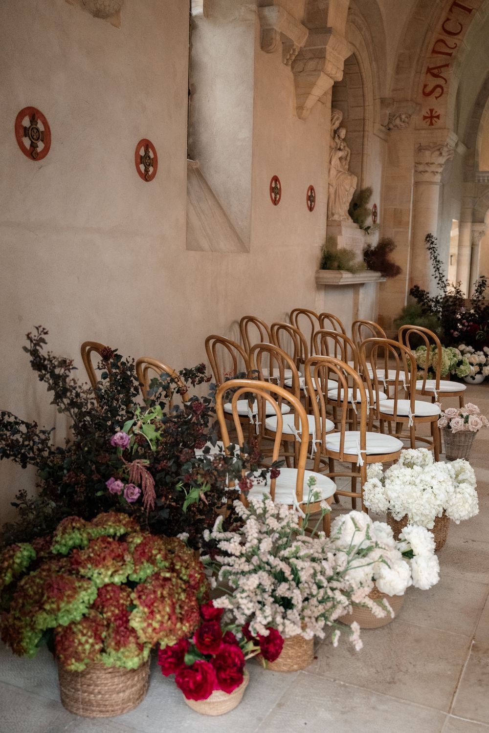 Stone church interior with wooden chairs and elaborate floral arrangements featuring roses and hydrangeas.