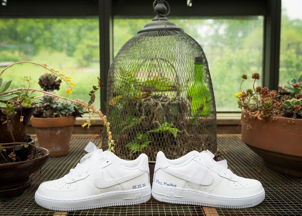 Custom white Nike Air Force 1 sneakers displayed on a windowsill surrounded by lush green plants.