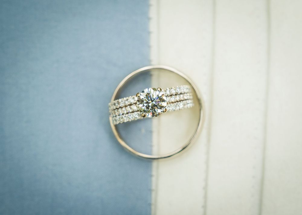 Diamond solitaire engagement ring with pavé band resting on blue and white striped fabric background.
