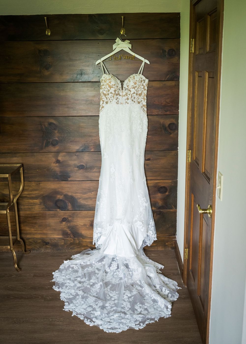 Elegant lace mermaid wedding dress with long train hanging on a wooden wall hanger.