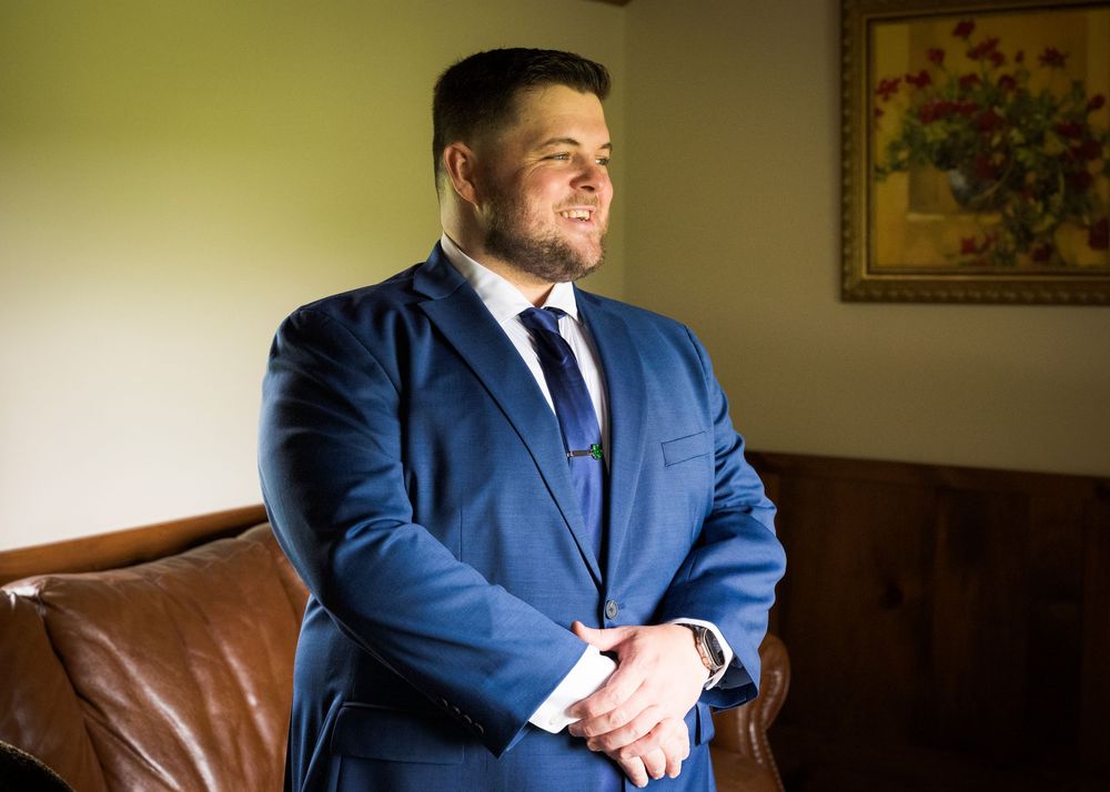 Groom smiling in a blue suit with tie while getting ready for his wedding ceremony.