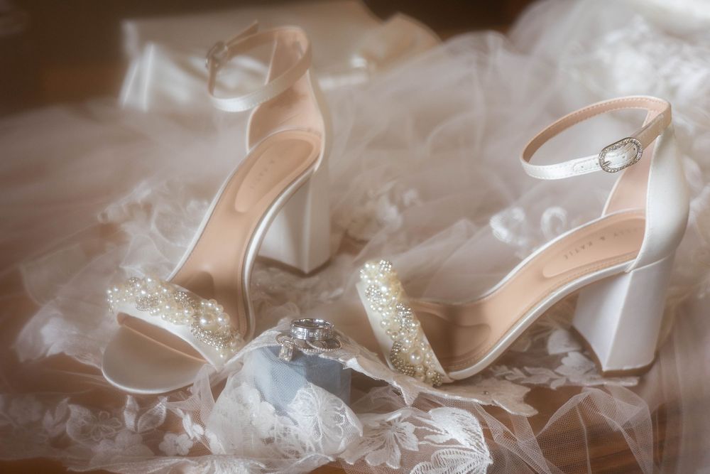 Elegant white bridal sandals with pearl embellishments and block heels rest on soft tulle fabric.