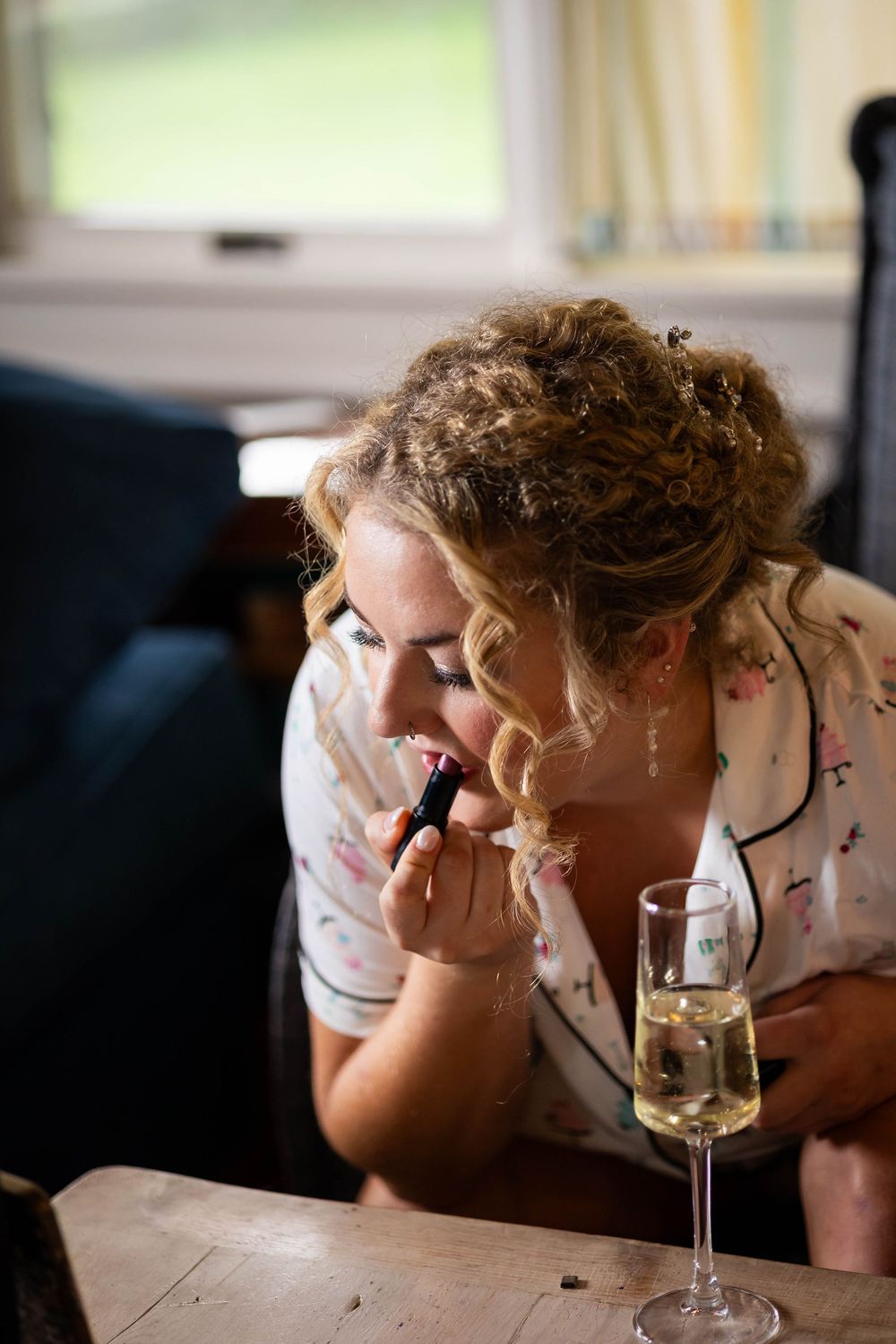 A bride in a robe drinking champagne putting her make up on before her wedding ceremony