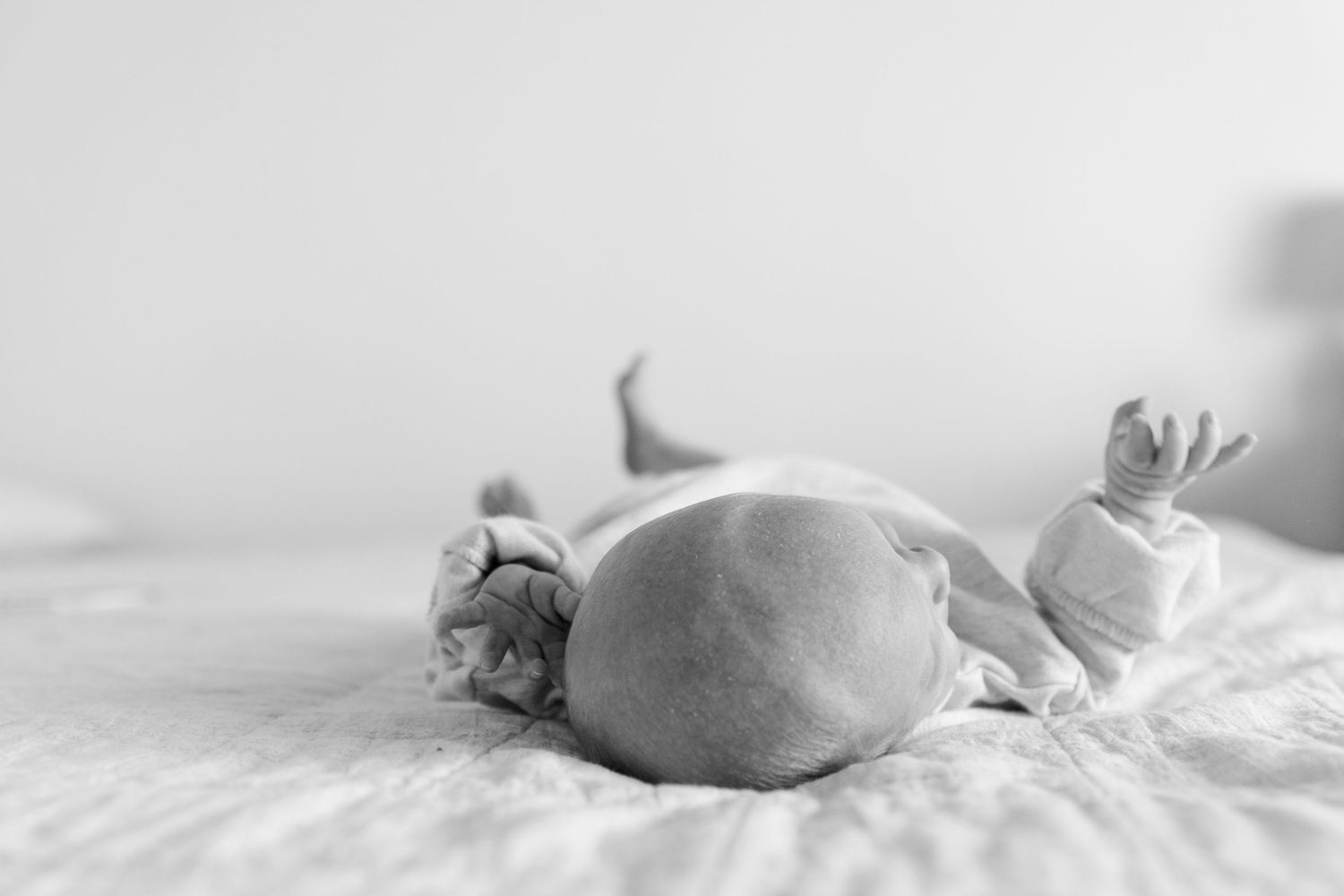 b&w baby laying on back on bed focus on the top of babies head