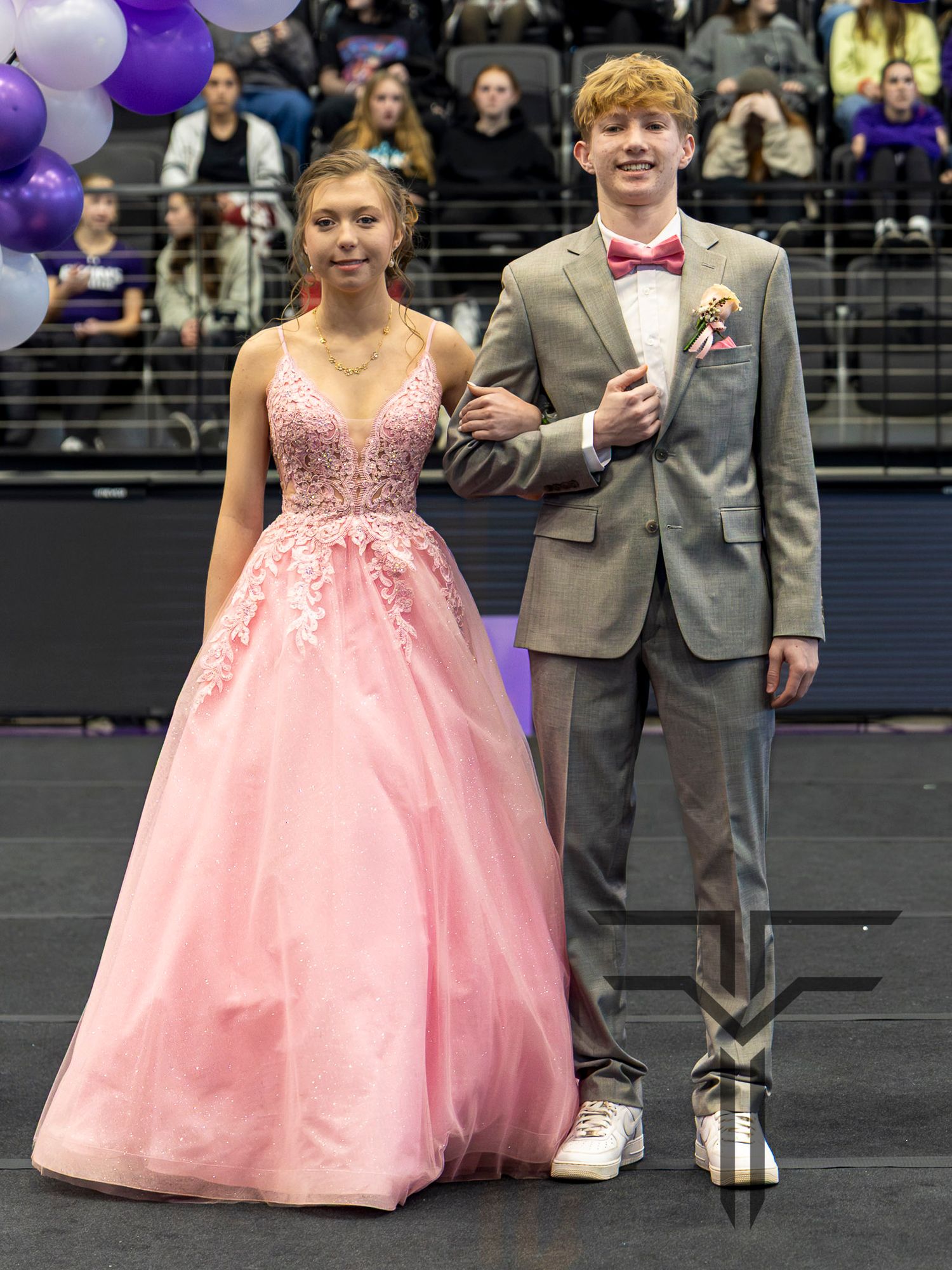 Teen couple in formal wear at prom, girl in pink ball gown and boy in gray suit with bow tie.