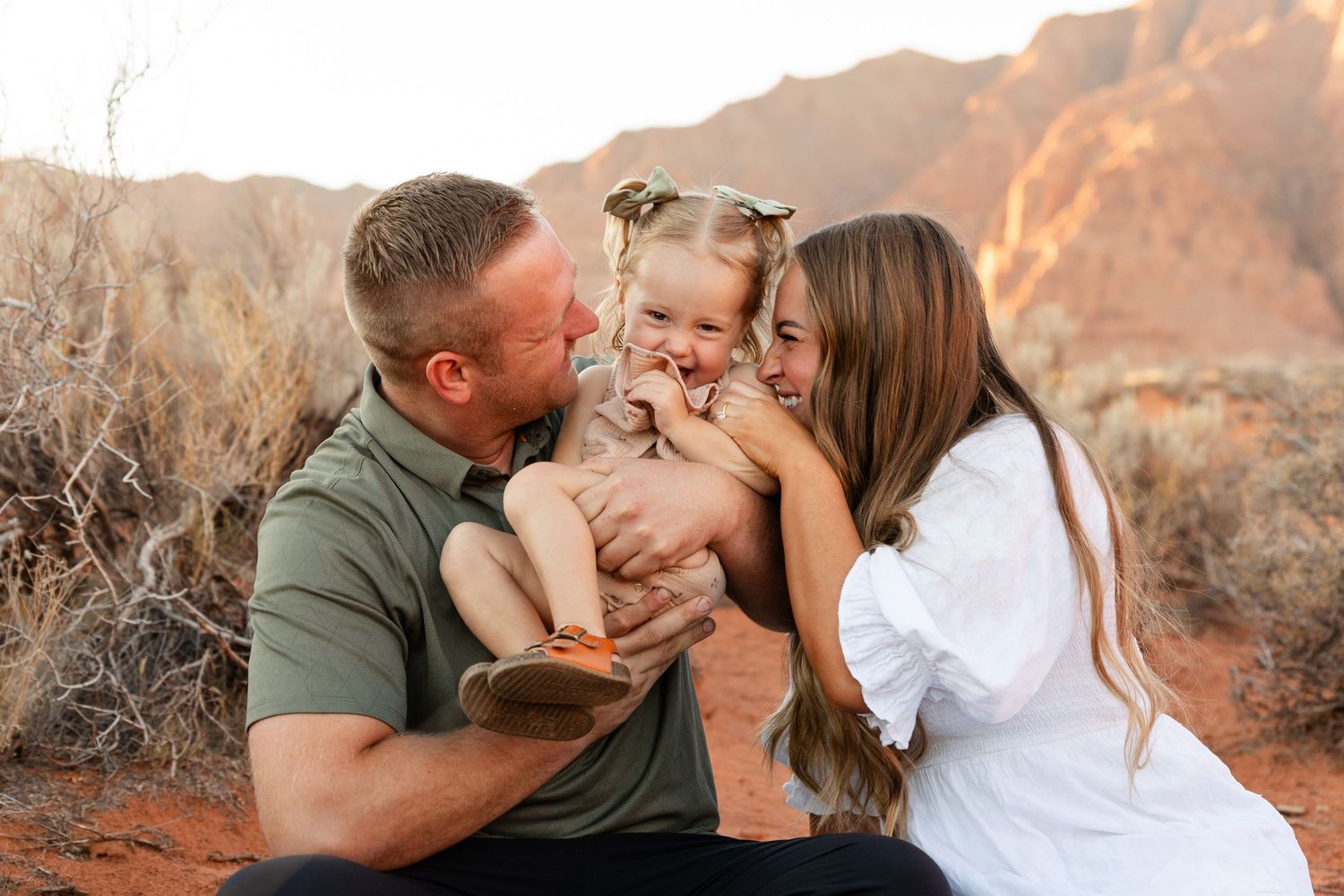 mom and dad tickling a little girl that's laughing between them.