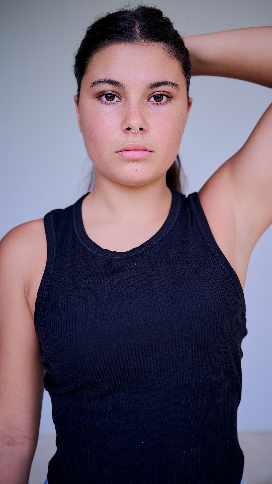 Model in white crop top and baggy blue jeans poses on black stool against light background in fashion photoshoot.
