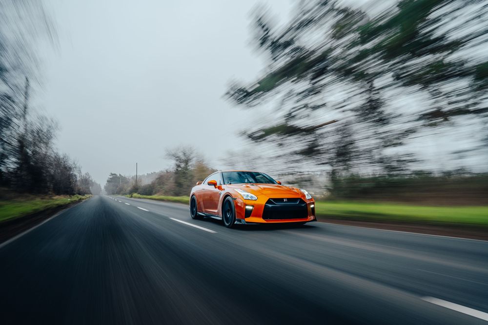 A series of motion-blurred road photos featuring a bright orange Nissan GTR driving through scenic landscapes.