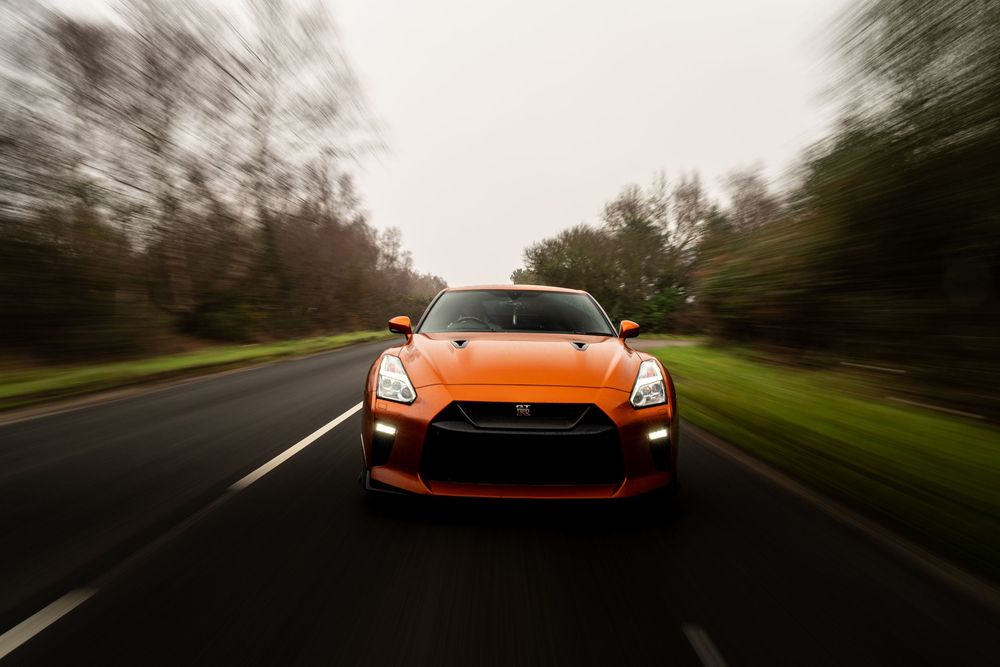 Orange Nissan GT-R sports car driving on a winding forest road at dusk with motion blur effect.