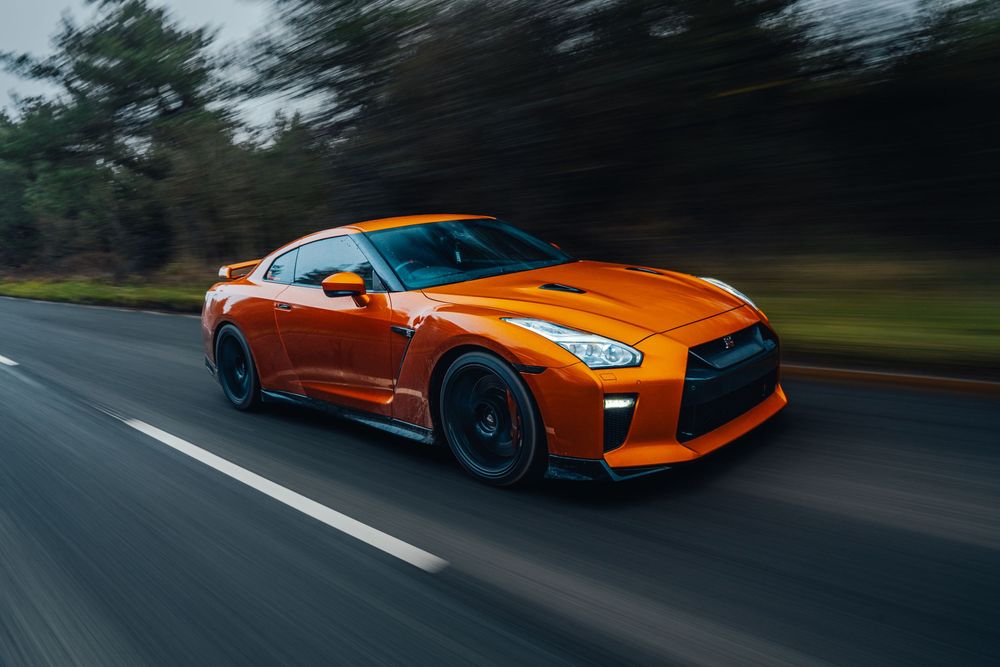 Orange Nissan GT-R racing through a curved road with dramatic motion blur and forest backdrop.