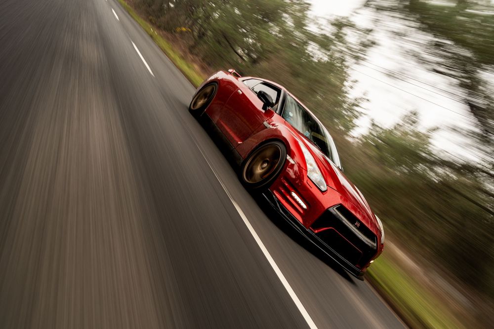 A red Ferrari sports car speeds down a winding forest road with motion blur effects in the background.