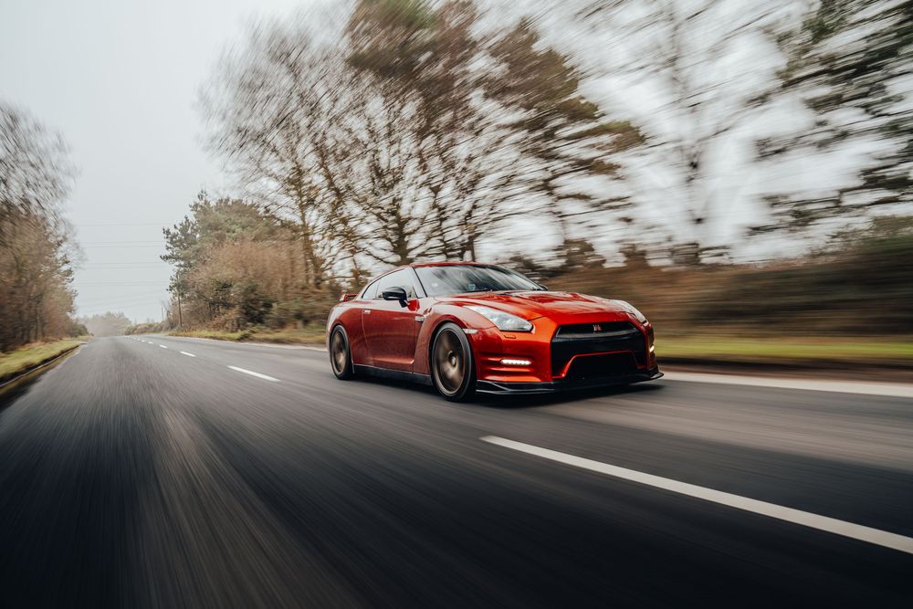 Motion-blurred shot of a red Nissan GT-R sports car driving on a curving road during daytime.