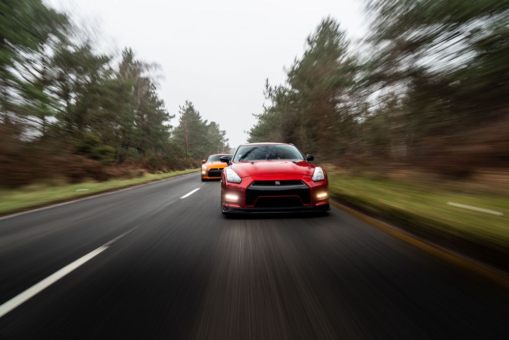 Red sports car driving fast on a winding forest road with motion blur effect creating a sense of speed and movement.