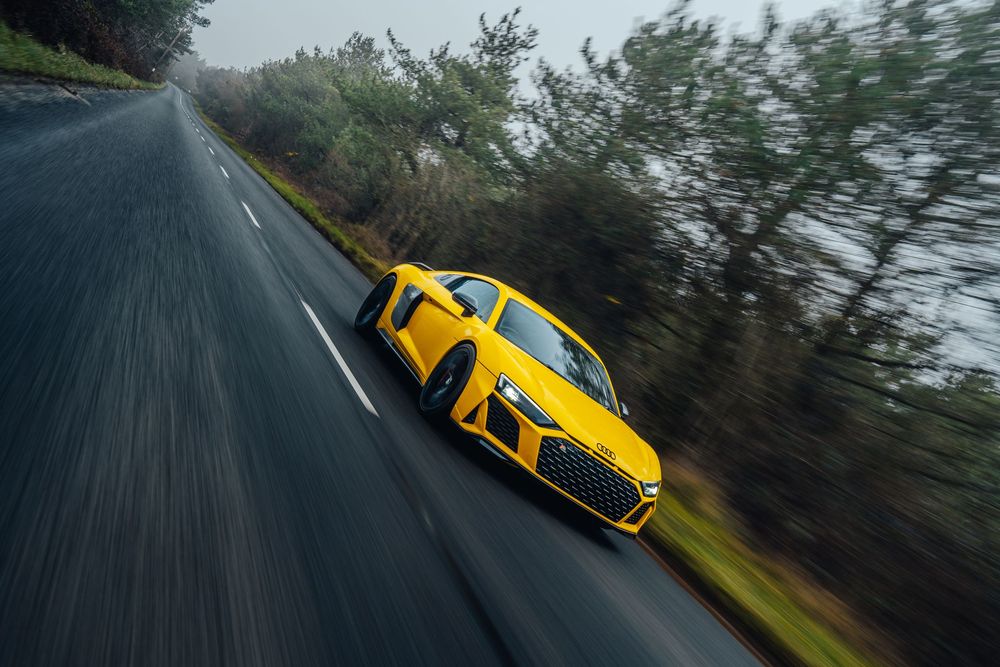 Yellow Audi R8 sports car driving on a winding mountain road through misty forest scenery.