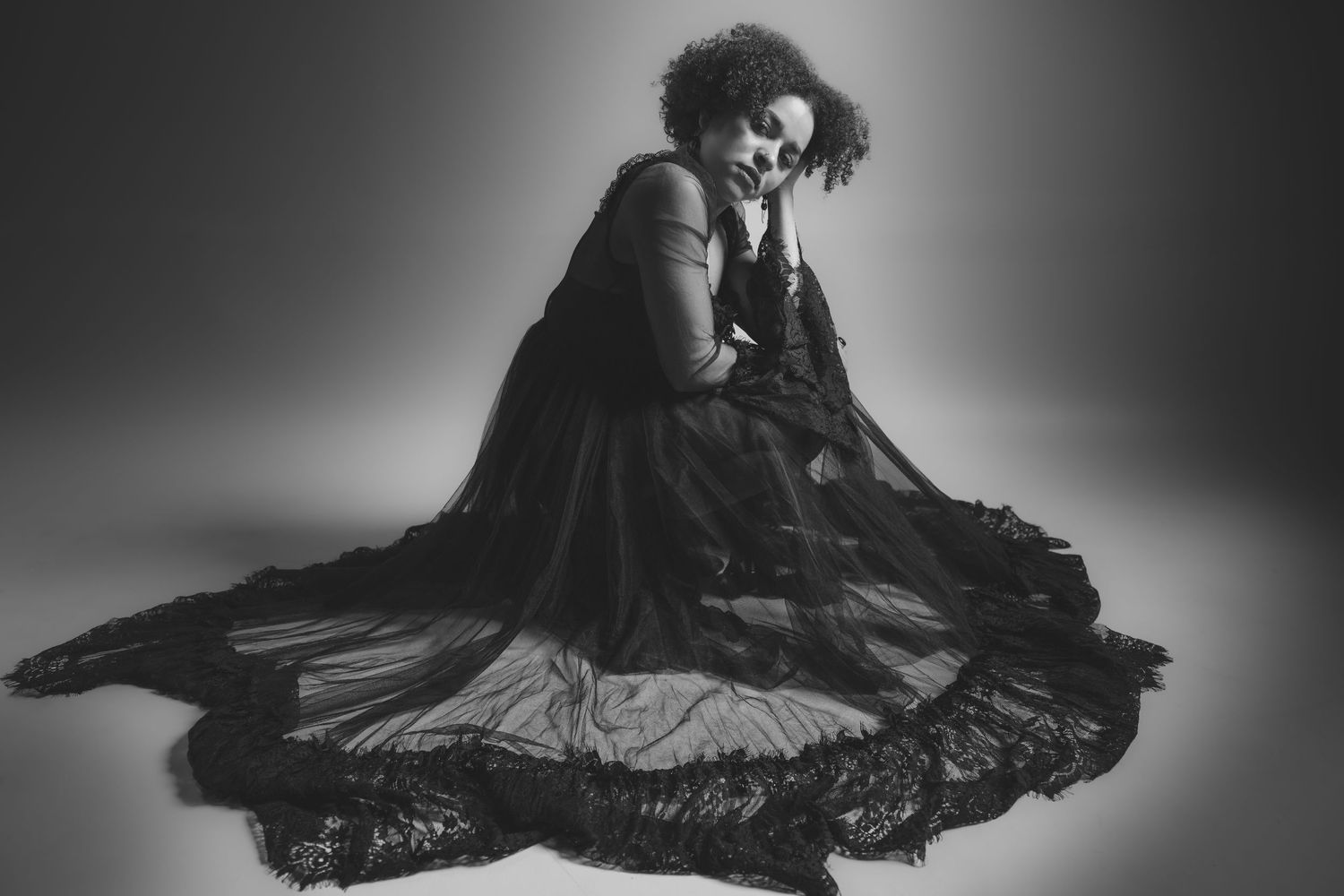 Graceful dancer in flowing black dress creates dynamic movement in monochromatic studio portrait.