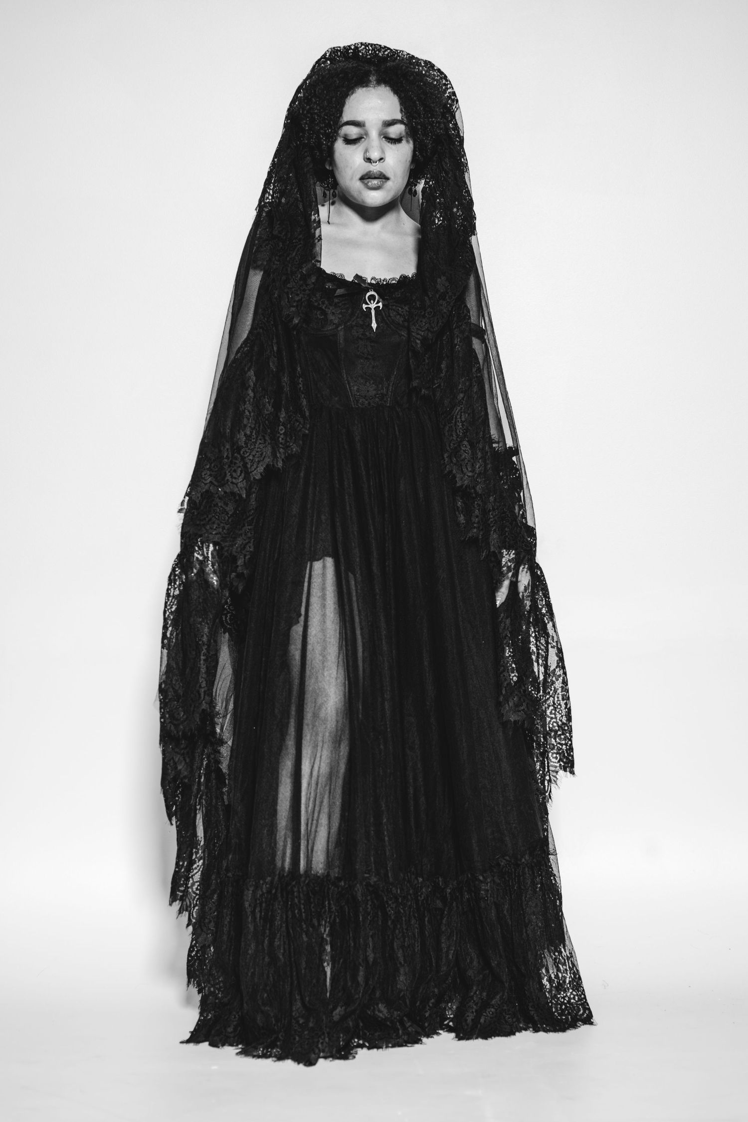 Gothic fashion photograph showing flowing black lace dress and veil against stark white background.