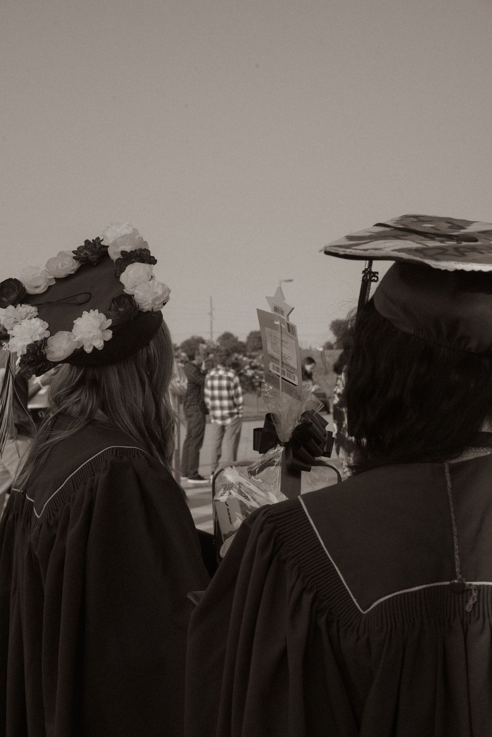 Black and white photo showing graduates in caps and gowns from behind.