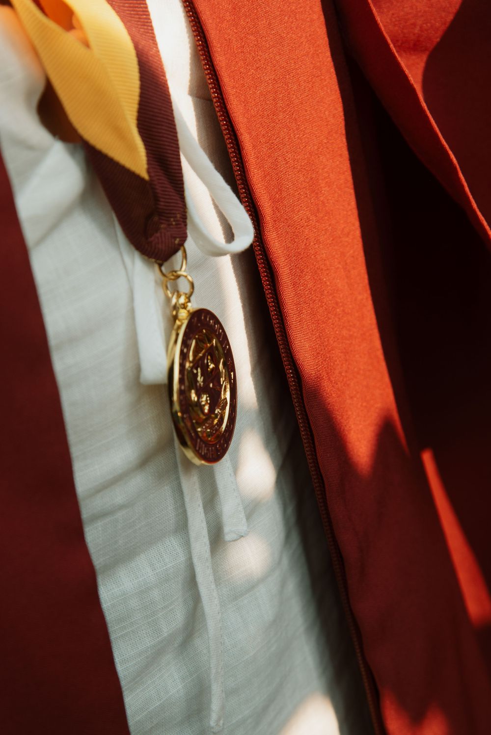 Detail shot of gold medallion on maroon graduation gown.