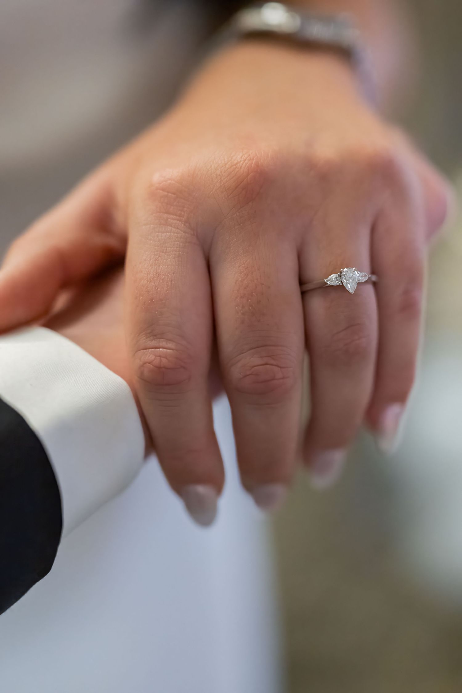 Close-up shot of an elegant diamond engagement ring on a hand against a white dress sleeve.
