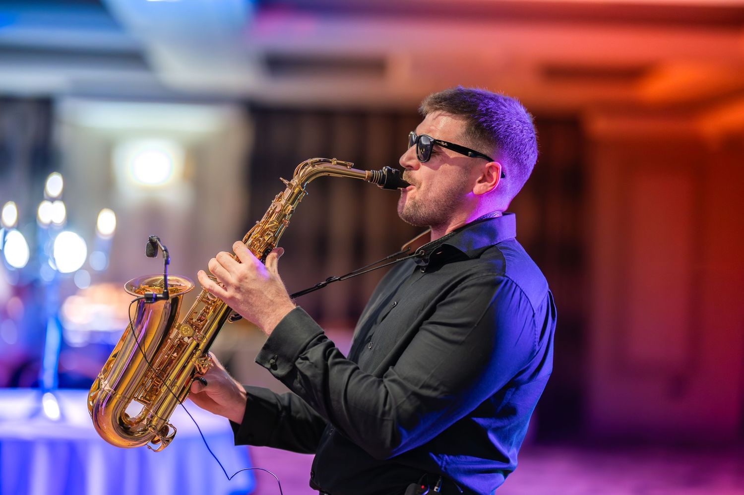Saxophone player performing on stage with dramatic blue and red lighting effects in the background.
