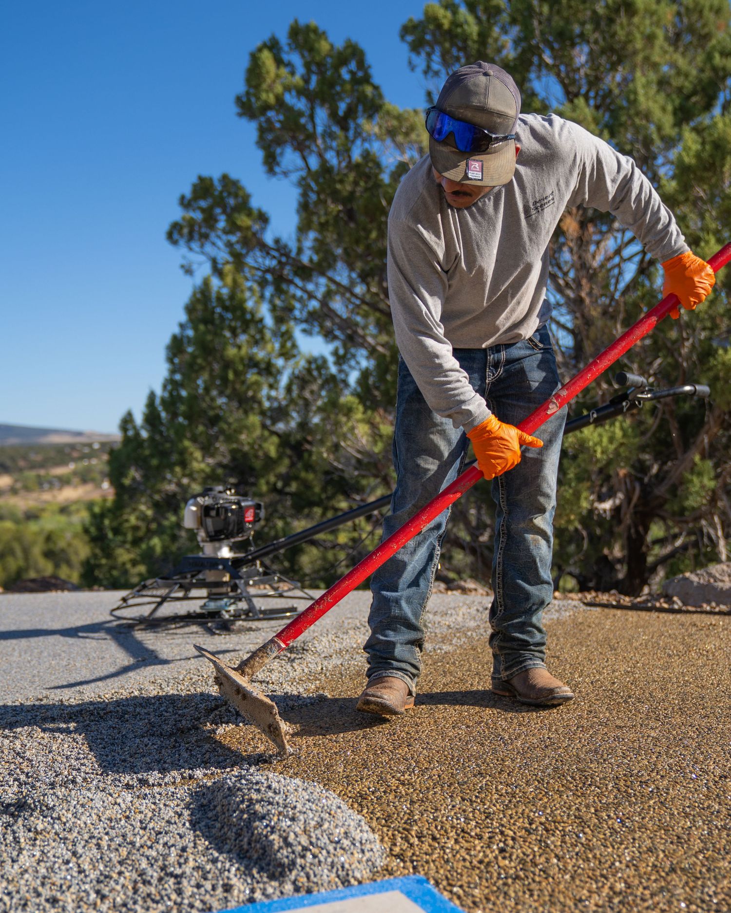 Person using red rake to spread and level decorative gravel in outdoor landscaping project.